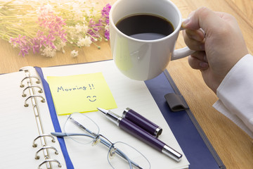 Businessman and a cup of coffee with opened notebook with Morning message on wooden background with pen, glasses and flowers. warm tone. warm tone.