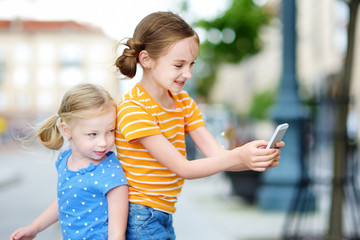 Two cute little sisters playing outdoor mobile game on their smart phones