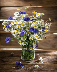 Bouquet of chamomiles and cornflowers in the vase on the wooden