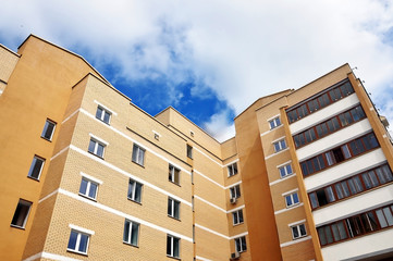 Look up at the modern multistory apartment building of beige brick against the cloudy sky.