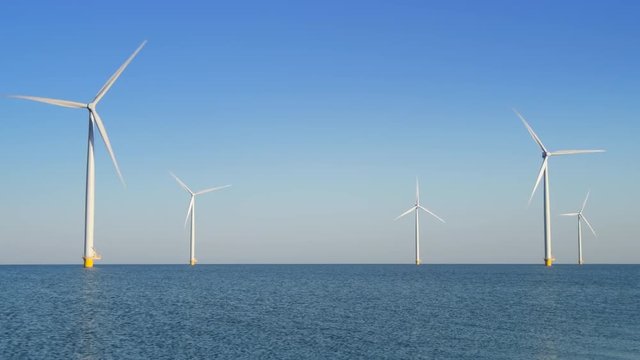 Wind turbines with rotating blades in an offshore wind park during a beautiful summer day.
