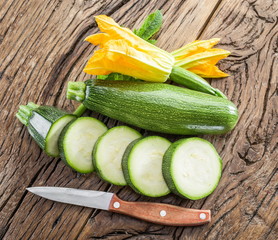 Zucchini with slices and zucchini flowers on a wooden table.