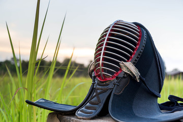 Used and Dirty Kendo Helmet or Men in grass field on sunset background.
