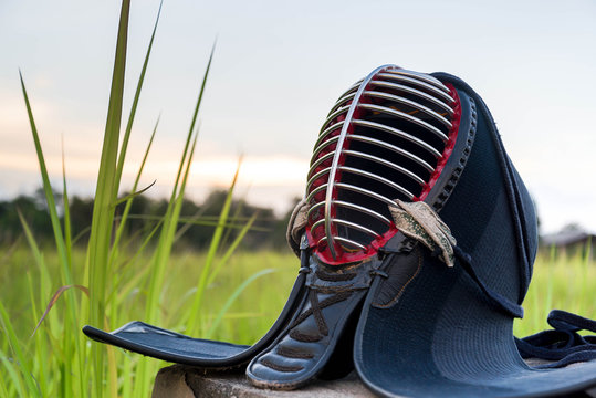 Used And Dirty Kendo Helmet Or Men In Grass Field On Sunset Background.