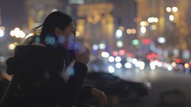 Young upset woman remembering ex-boyfriend and drinking tea in night city center