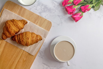 Breakfast with croissants, pink rose flower, cutting board and b