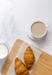 Breakfast with croissants, milk, cutting board and black coffee