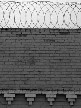 Black and white image of brick wall with barbed wire on top