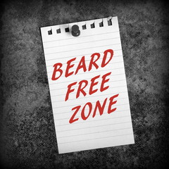 The phrase Beard Free Zone in red text on lined paper pinned to a grunge background processed in black and white for effect