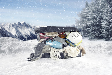 Winter clothing and ski accessories stuffed and spilling out of a large suitcase placed on a snowy...