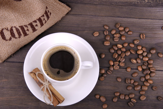 Coffee cup, beans and jute bag on wood background
