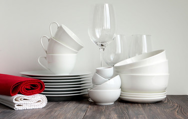 White dishware stacked on a wooden table against black background with transparent wineglasses and rolled layovers