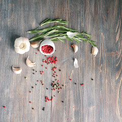 Pink pepper spilled on a wooden table with rosemary, garlic bulb and cloves

