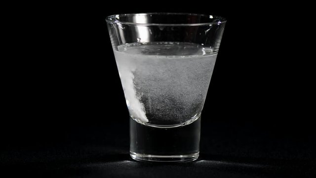 Dissolving one pain killer preparation tablet in glass of water against a black background.