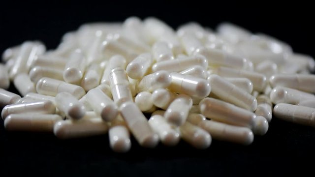 Large pile of white capsules on black background, close up.