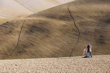 Photographer on plough Tuscany field with Furrows in curved Lines