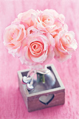 Artificial Pink Roses in a vase on a pink background.