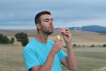 Young man blowing soap bubbles in the summer outdoors
