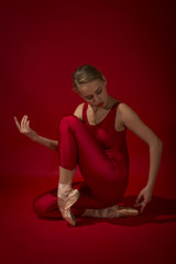 Fototapeta na wymiar Ballerina in red outfit posing on toes, studio shot on red background. Young beautiful dancer posing in studio
