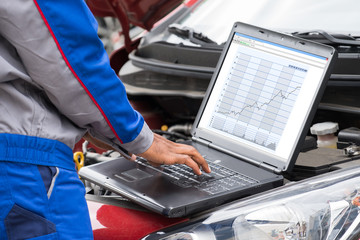 Mechanic Using Laptop For Examining Car Engine