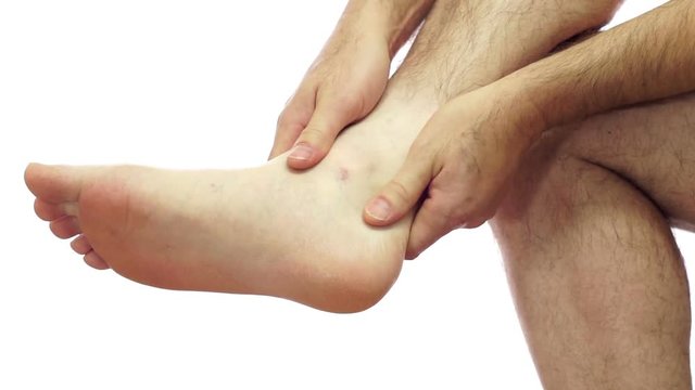Closeup of an anonymous man isolated on a white background and rubbing his sore and painful foot ankle joint.