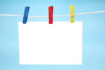 Colorful clothes pegs holding empty note against blue background