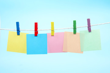 Colorful clothes pegs holding colorful notes against blue background