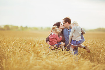 Mother and father holds on a hands their little children and kiss each other on a field