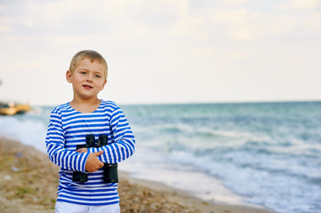 The little boy in the vest with the binoculars , walks on the beach