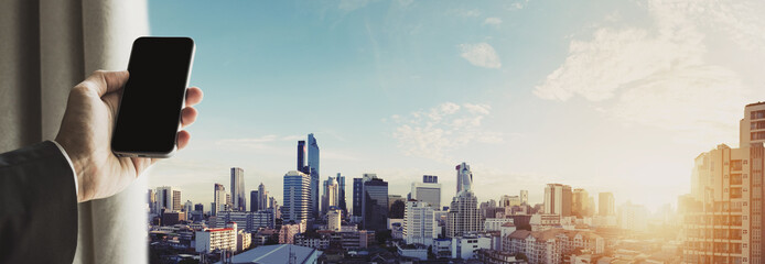 Hand holding mobile phone with panoramic cityscape of Bangkok city in sunrise, vintage tone