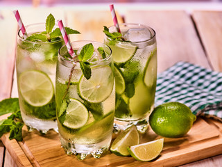 Alcohol straw cocktail. On wooden boards three glasses with alcohol drink and ice cubes. Drink number two hundred twenty nine cocktail mohito and checkered napkin. Country life. Light background.