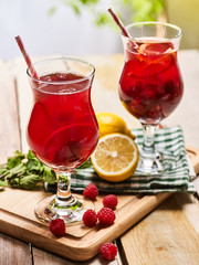 On wooden boards two red ice cold beverage glasses with red raspberry lemon cocktail . Alcohol country cocktail beverage number two hundred thirty nine with checkered cloth. Top view cocktail outdoor.
