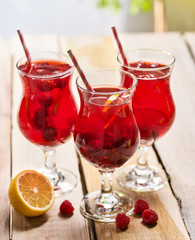 On wooden boards are three ice cold beverage glasses with red raspberry lemon cocktail . Alcohol country cocktail beverage number two hundred fourty with lemon. Group of raspberry cocktail on outdoor.