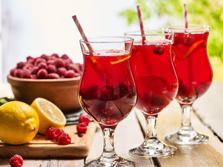 On wooden boards three ice cold beverage glasses with red raspberry lemon cocktail . Alcohol country cocktail beverage number two hundred fourty one with raspberry basket. Lemon cocktail on outdoor.