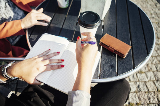 Cropped image of businesswoman writing in diary at sidewalk cafe table