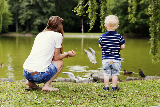 Rear view of mother and son feeding ducks on pond