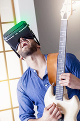 young adult playing guitar at home using viewer for virtual real