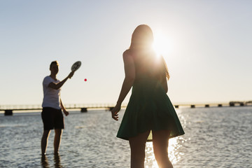 Couple playing tennis at shore against clear sky during sunset