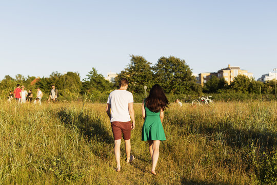 Rear view of couple walking on grassy field against clear sky