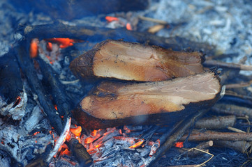 Pieces of smoked bacon being cooked on bonfire
