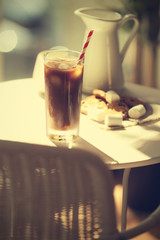 Iced coffee with straw on white table in cafe