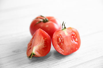 Red juicy tomato and slices on light wooden background
