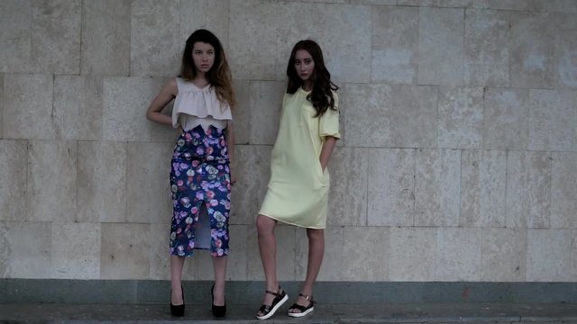 Two attractive young woman posing near wall for fashion photographer