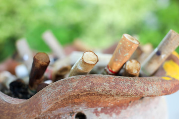 Cigarette butts in the clay pot with green background