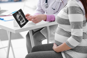 Young pregnant woman visiting doctor and looking at ultrasound photo