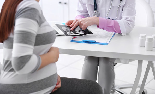 Young pregnant woman visiting doctor and looking at ultrasound photo