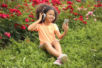 Afro-American little girl with headphones listening to music in park