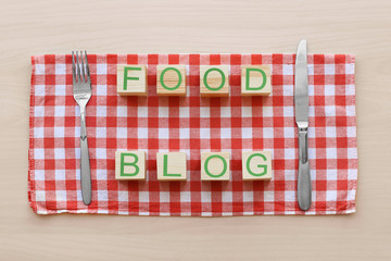 Fototapeta premium Food blog wooden blocks with fork and knife on red gingham tablecloth, culinary content creation