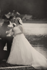 Fototapeta premium Gromm kisses bride's cheek standing on the lake's shore