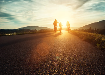 Ð¡yclists family traveling on the road at sunset